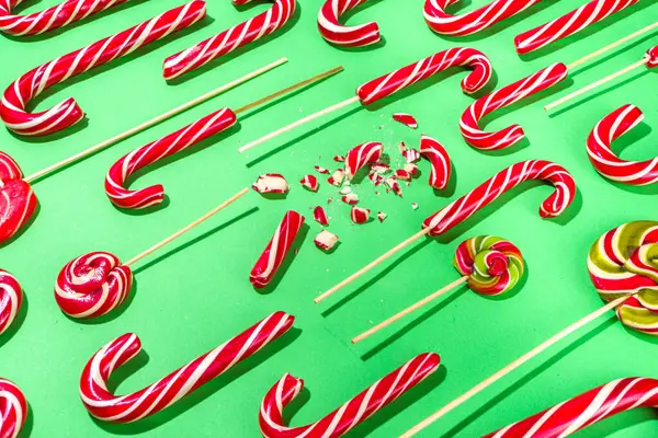 Deconstructed candy cane flatlay. Christmas Deconstruction Background with whole and shattered into pieces and shards candy cane sweets on high-colored green background flatlay, Xmas pattern