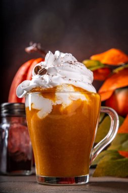 Bir sürü krem şanti ve kahve çekirdeği dekoru olan cam bardakta balkabağı baharatlı latte. 