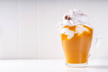 Bir sürü krem şanti ve kahve çekirdeği dekoru olan cam bardakta balkabağı baharatlı latte. 