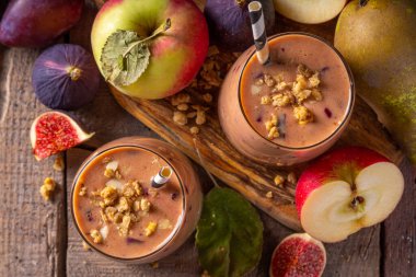 Sonbahar meyveli yoğurt içeceği. Taze meyve, erik, incir, elma, yulaf ve fındık, ahşap arka plan fotokopi alanı ile iki bardak çırpılmış meyve suyu.