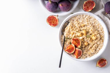 Sonbahar kahvaltısı sabah yulaf ezmesi. Beyaz mutfak arka planında taze incir ve fındıklı bir kase yulaf ezmesi.