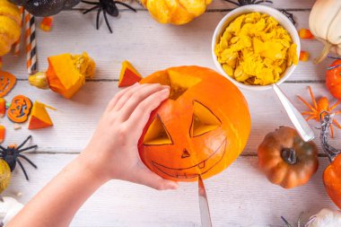 Balkabağı oyma Jack Feneri ile Cadılar Bayramı hazırlığı. Kadın, kadın ve çocuklar ellerini çerçeveye koyar, dekore eder, çizer ve korkunç Cadılar Bayramı partisini oyar.