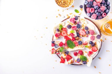 Ev yapımı donmuş yoğurt kabuğu, Yunan yoğurdundan yapılan alternatif sağlıklı keto diyeti dondurması, taze böğürtlen, fındık, granola, bal, fırın tepsisi deco. Meyve soslu donmuş yoğurt.