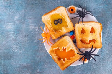 Cadılar Bayramı için komik çocuk yemekleri, atıştırmalık ya da brunch sandviçleri kızarmış ekmek, geleneksel Cadılar Bayramı canavarları şeklinde peynir - balkabağı, fener, hayalet, yarasa, mavi masa üzerinde bayram dekoru