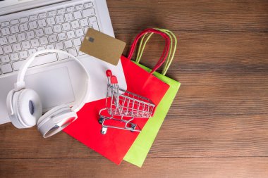 İnternetten Noel alışverişi yapıyorum. Kış Xmas çevrimiçi satışı. Kulaklıklı beyaz laptop, alışveriş arabası ve çantalar, kredi kartı ahşap arka plan kopyalama alanı