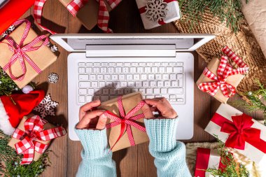 Tahta arka planda Noel hediyesi kutuları olan dizüstü bilgisayar kullanan biri. Kadın eli hediyeli defter, köknar ağacı ve kış dekoru. Noel ve Yeni Yıl için Hazırlık