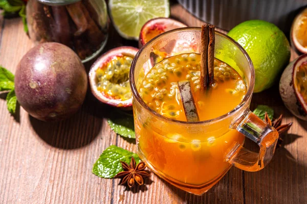 Passion fruit hot tea drink with fruity juice, cinnamon, lime, over wooden background with fresh passion fruit and spices