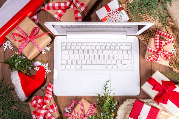 Laptop computer with Christmas gift boxes from above on wooden background. Notebook with presents, fir tree and winter decor. Preparation for Christmas, New Year