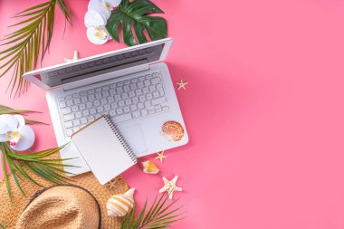 Yazlık ofis, çalışma geçmişi, blogcu iş yeri düzlüğü. Not defteri, hasır şapka, tropikal dekor ve yapraklarla dolu beyaz dizüstü bilgisayar klavyesi, açık pembe arka planda soğuk kokteyl bardağı.