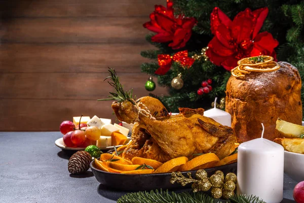 Christmas or New Year dinner foods on dark table. Set of traditional Xmas party dishes - pannetone, baked chicken, vegetables, potato, cheese and fruits plate, top view copy space