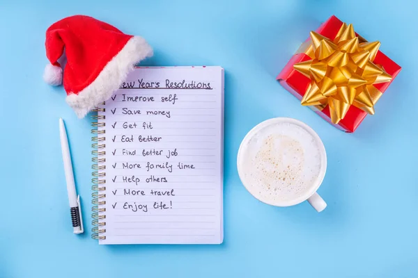 New Year plan goals List on notebook with Santa hat, coffee latte or hot chocolate cup, simple New Year goals List 2023, plan listing of new year beginnings goals flat lay background, banner