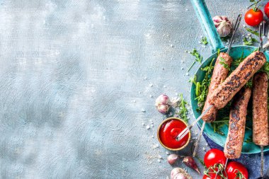Şişe şiş kebap, kıyma etinden. Lula kebap, geleneksel Kafkas tarifi. Mavi beton arka planda, soslar, domatesler ve sebze salatası üst görünüm fotokopi alanı