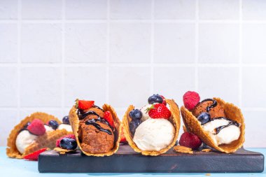 Çeşitli tatlı taco dondurmaları. Çikolata ve vanilya aromalı waffle kabukları. Farklı meyveler, meyveler, malzemeler.