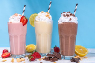 Yaz tazeleyici milkshake seti ya da klasik lezzetli tadı olan meyve suları vanilya limonu, çilek, çikolata, krem şanti ve malzemelerle beyaz, açık mavi, güneşli bir arka planda. 