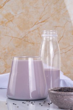 Siyah ve beyaz susam sütü, süt içermeyen alternatif vejetaryen süt bardakta ve ışık taşı zemininde susam tohumu olan şişelerde. Çiğ yiyecek, vejetaryen doğal gıda diyeti.