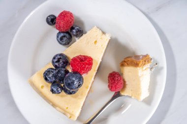 Tabakta peynirli kek dilimi, beyaz mermer zemin üzerinde ahududu. 