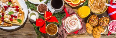 Festive Christmas morning breakfast or brunch table, with traditional food  pancakes, Belgian waffles, fried eggs, croissant, stolen, cookies, with orange juice and coffee, cinnamon rice porridge 