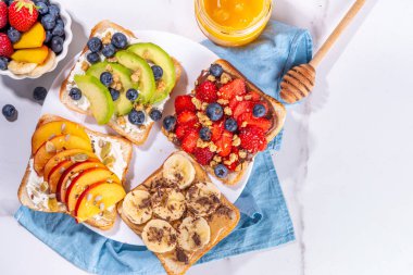 Meyveli sandviç. Fıstık ezmeli, krem peynirli çeşitli tostlar, yaz meyveleri ve meyveli çikolata - çilek, muz, şeftali, elma, yabanmersini, lezzetli öğle yemeği