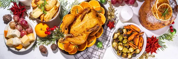 Christmas or New Year dinner foods on white wooden table. Set of traditional Xmas party dishes - pannetone, baked chicken, vegetables, potato, cheese and fruits plate, top view copy space