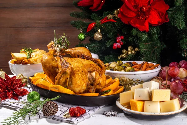 Christmas or New Year dinner foods on white wooden table. Set of traditional Xmas party dishes - pannetone, baked chicken, vegetables, potato, cheese and fruits plate, top view copy space