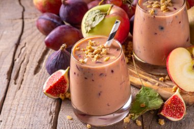 Sonbahar meyveli yoğurt içeceği. Taze meyve, erik, incir, elma, yulaf ve fındık, ahşap arka plan fotokopi alanı ile iki bardak çırpılmış meyve suyu.