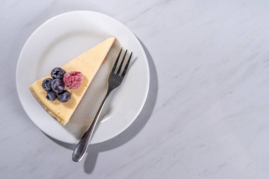 Tabakta peynirli kek dilimi, beyaz mermer zemin üzerinde ahududu. 