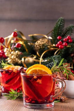 Geleneksel Noel aromalı şarap kokteyli, baharatlı kırmızı şarap içkisi, tarçın, portakal ve biberiye filizleri, Noel süslenmiş ahşap kaplama arka planda.