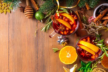 Geleneksel Noel aromalı şarap kokteyli, baharatlı kırmızı şarap içkisi, tarçın, portakal ve biberiye filizleri, Noel süslenmiş ahşap kaplama arka planda.