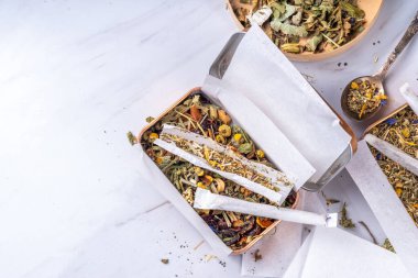 Alternatif sağlıklı berbal sigara karışımı. El yapımı sigara, hazırlık süreci, bitki, yaprak ve çiçek karışımı, kutular, kağıt, beyaz arka plan