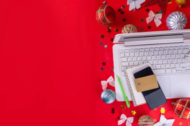 Yılbaşı arkaplanında beyaz dizüstü bilgisayar klavyesi ve kış tatili dekorasyonu parlak kırmızı arka planda süsleri var. Noel alışverişi, tatil hazırlıkları, üst görünüm kopya alanı