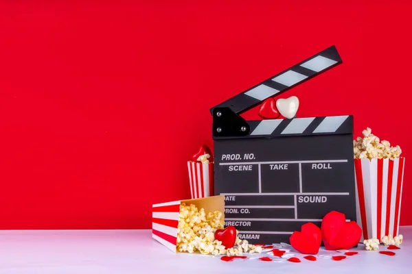 2月14日のバレンタインデーのロマンチックな日付 映画マラソンを愛し 映画館でデートする クラッパーボード ポップコーンバケツ ハートデコレーション 赤い背景フラットレイコピースペースでのチョコレート — ストック写真
