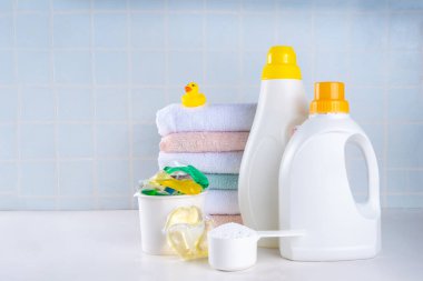 Çamaşır, çamaşır ve temizlik konsepti. Bir yığın temiz havlu, çeşitli deterjanlar - jeller, kapsüller, toz, çamaşır sepeti ve sevimli sarı ördek, beyaz banyo arka plan fotokopisi