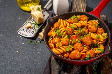 Domates soslu köfteli fusilli makarna, koyu arkaplanda otlar ve rendelenmiş peynir, üst görünüm fotokopi alanı