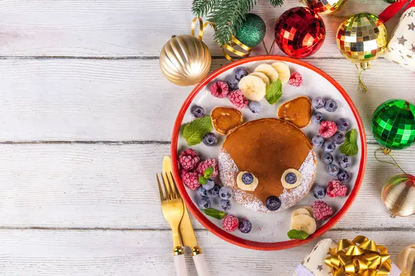 stock image Funny and cute Christmas little fox pancakes on a red white plate decorated with fresh berry, fruit and powdered sugar, children's Christmas breakfast or brunch idea