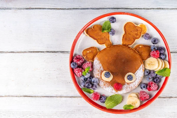 stock image Funny and cute Christmas reindeer pancakes on a red white plate decorated with fresh berry, fruit and powdered sugar, children's Christmas breakfast or brunch idea