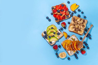 Meyveli sandviç. Fıstık ezmeli, krem peynirli çeşitli tostlar, yaz meyveleri ve meyveli çikolata - çilek, muz, şeftali, elma, yabanmersini, lezzetli öğle yemeği