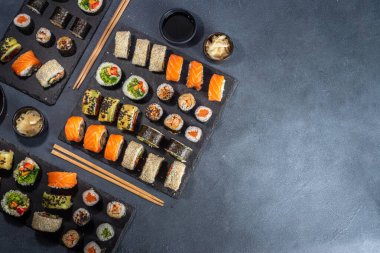 Suşi, soya sosu, zencefil ve yemek çubuklarıyla birlikte koyu arkaplan üzerine kuruludur.