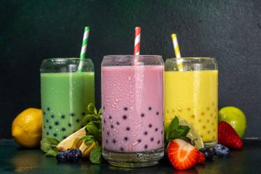 Üç renkli yaz köpüklü çay seti, parlak kremalı inci çayı ya da latte tapyoka içecekleri, pembe dut, sarı narenciye, yeşil nane, tapyoka topları ve ezilmiş buz, koyu arkaplanda.