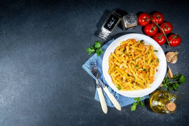 İtalyan Akdeniz yemek konsepti. Deniz ürünleri, karides, sebze ve kremalı soslu Fusilli makarna. Siyah beton masanın üzerinde, akşam yemeği için baharatlar var.