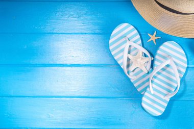 Bright sunny lighted summer vacation background, vacation and travel, beach accessories, swim suit, hat, flip flops, photo camera, sea star and shells on high-colored blue wooden background top view