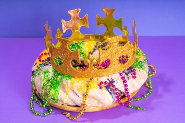 King Cake for Mardi Gras, traditional New Orlean Mardi Gras holiday pastry with plastic baby, with festival masquerade accessories, decor, carnival mask, beads