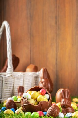 Easter egg hunting background. Various candy and chocolate Easter eggs, bunny and rabbits with basket for eggs on green grass park or garden background