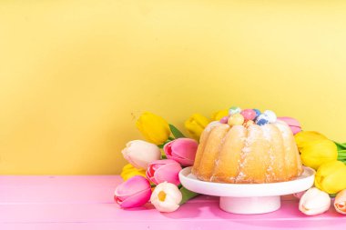 Geleneksel Paskalya yuvarlak pastası. Tatlı geleneksel Paskalya pişirmesi şeker tozu serpintileri, renkli Paskalya yumurtaları, bahar çiçekleri, pembe sarı renkli arka plan fotokopi alanı