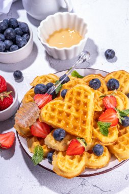 Çilekli, yaban mersinli ve ballı Belçika waffle 'ları, beyaz mutfak masalarında ev yapımı kalp şeklinde waffle' lar.
