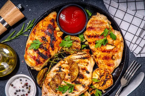 Grilled roasted chicken, turkey fillet. Spicy bbq fried white meat boneless fillet with garlic, rosemary, lemon and ketchup sauce, on black concrete table background top view copy space