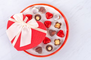 Sevgililer Günü tebrik kartı. Galentine tatil geçmişi. Kalp şeklinde hediye kutusu, kalp çikolatalı tatlılar ve beyaz arka planda kırmızı güller olan şekerler. Metin için en üst görünüm kopyalama alanı