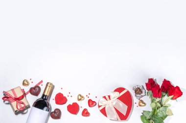Valentine's Day greeting card flat lay. Valentine day isolated white background with wine bottle, heart sweets chocolates, bouquet of red roses, gift box, heart shaped candies, confetti, beads 