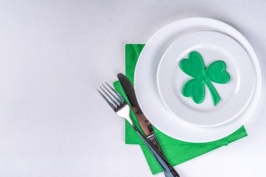 St. Patrick's Day festive table setting. Plate and cutlery with green napkin, shamrock symbol, gold horseshoe decor for luck. Patrick Day menu background, party invitation, top view copy space