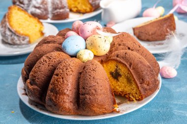 Traditional cake for Easter. Chocolate and vanilla Easter round cake with chocolate and sugar powder sprinkles, colorful Easter eggs, spring flowers, on a blue background copy space