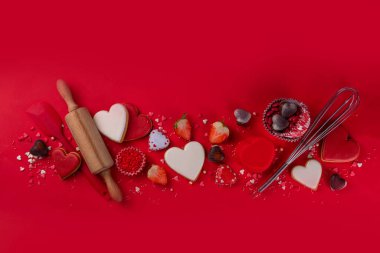 High-colored bright red Valentine day baking background, Various bakery ingredients, cookies, chocolates, sugar sprinkles, strawberry, rolling pin and whisk, for cooking valentine`s sweets, desserts